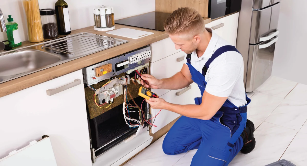 Technician using a multimeter to diagnose an open dishwasher under a kitchen counter
