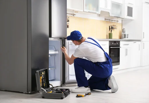 Technician inspecting a refrigerator freezer compartment with repair tools nearby