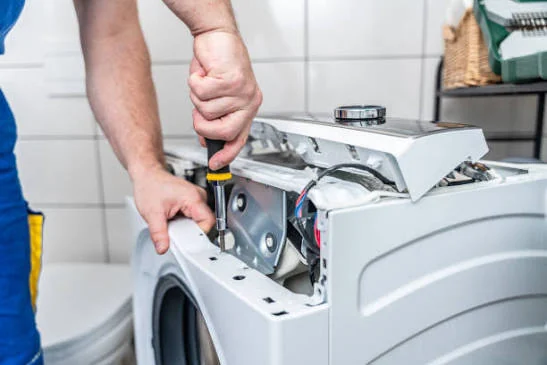 Close-up of a technician using a screwdriver on an opened laundry appliance