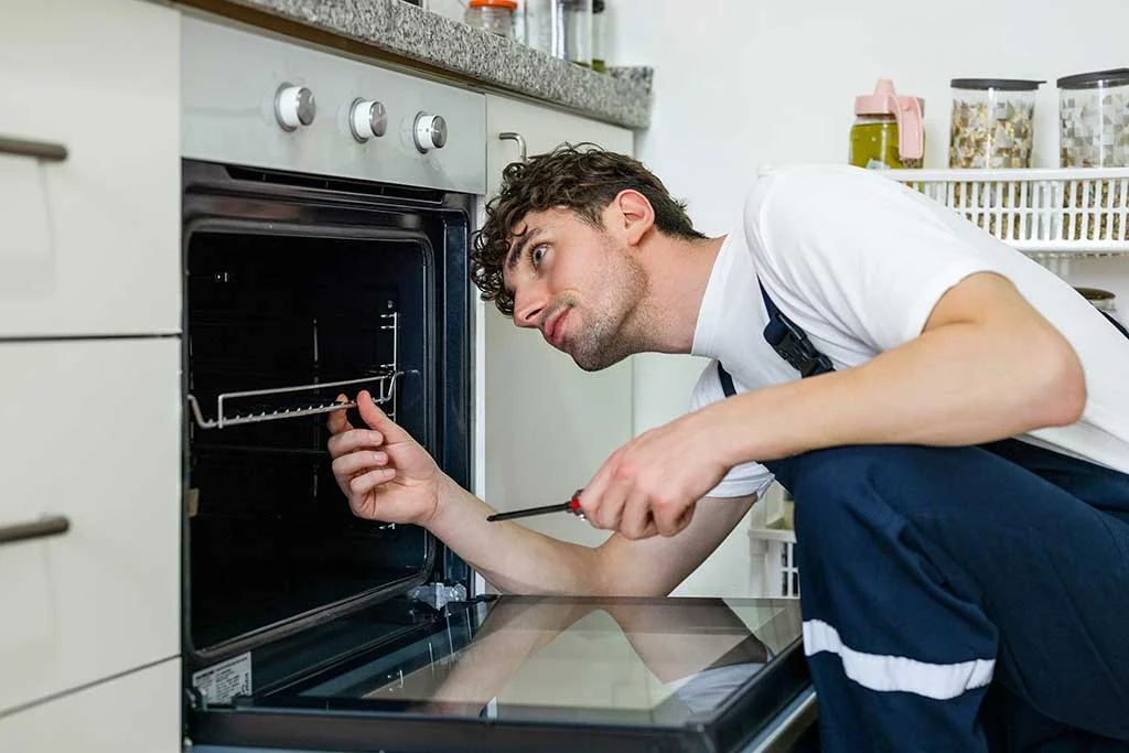 Technician inspecting an open built-in oven with a screwdriver