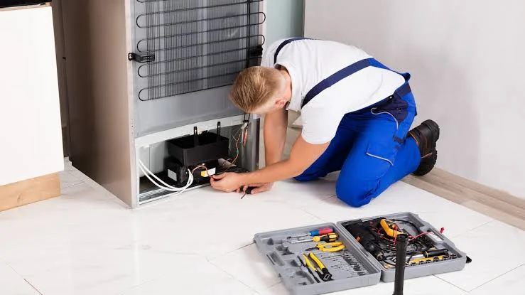 Technician checking the compressor and cooling components behind a refrigerator